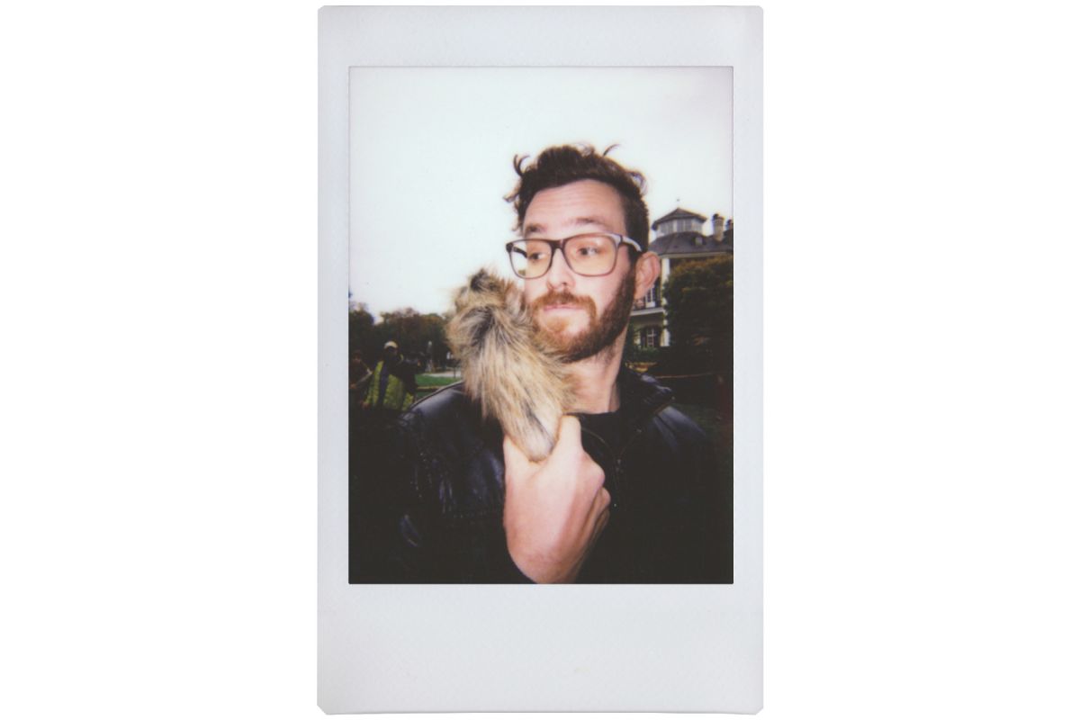 lomo instant mini film picture of a young man with glasses, holding a hairy object taken on fujifilm instax